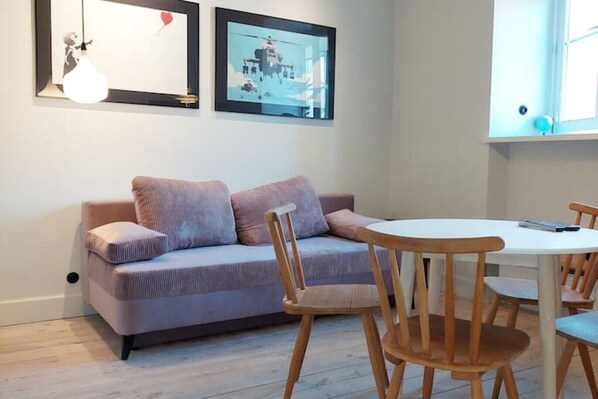 A room with a sofa, a round table, and chairs. There are framed pictures on the wall.