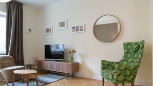 A living room with a flat-screen TV, a sofa, a chair, a small table, and a mirror on the wall. - Joanna's Studio Apartment Warsaw Old Town Rycerska street (Warszawa)
