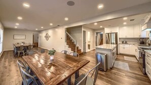 A spacious kitchen with a wooden dining table, stainless steel appliances, and a staircase leading to another level.