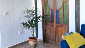 Une pièce avec un plafond en bois, une plante en pot, une chaise bleue avec un coussin jaune et une porte en bois dotée de panneaux de verre.