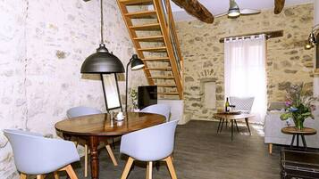 A rustic room with a wooden dining table, white chairs, a ladder, a fireplace, and a small round table with a vase of flowers.
