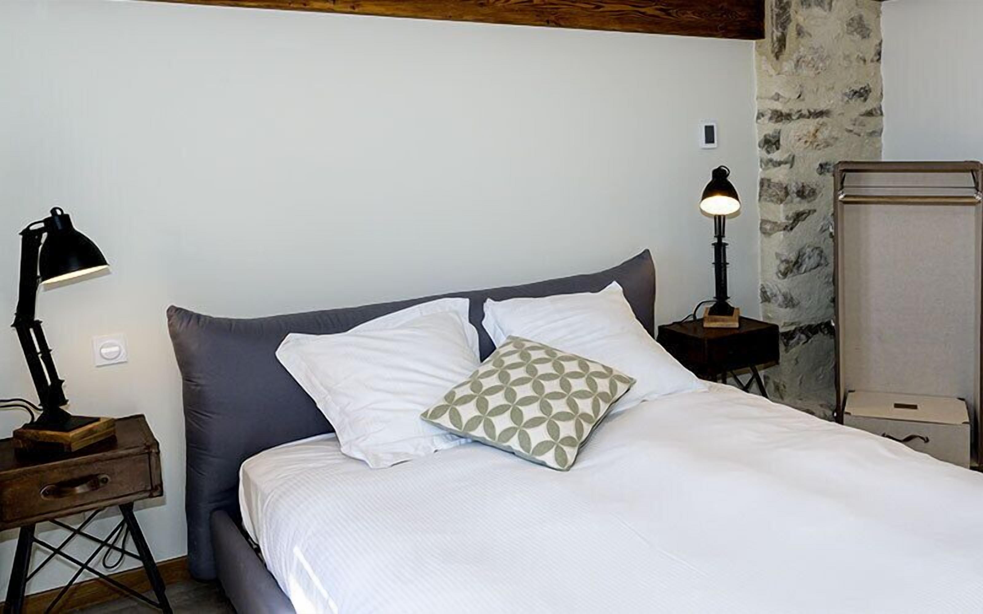 A neatly made bed with white and gray bedding, a patterned pillow, and two bedside lamps.