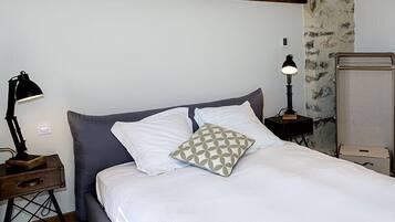 A neatly made bed with white and gray bedding, a patterned pillow, and two bedside lamps.