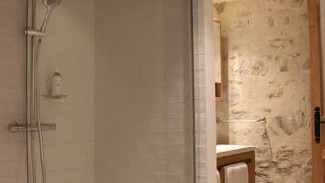 A glass-enclosed shower with a handheld showerhead and a wall-mounted faucet.