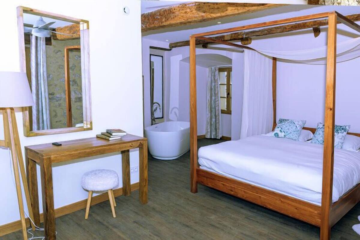 A bedroom with a four-poster bed, a wooden desk, a white lamp, and a large mirror.