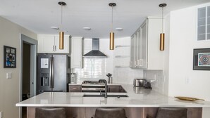 A modern kitchen with a central island, stainless steel appliances, pendant lighting, and a large window.