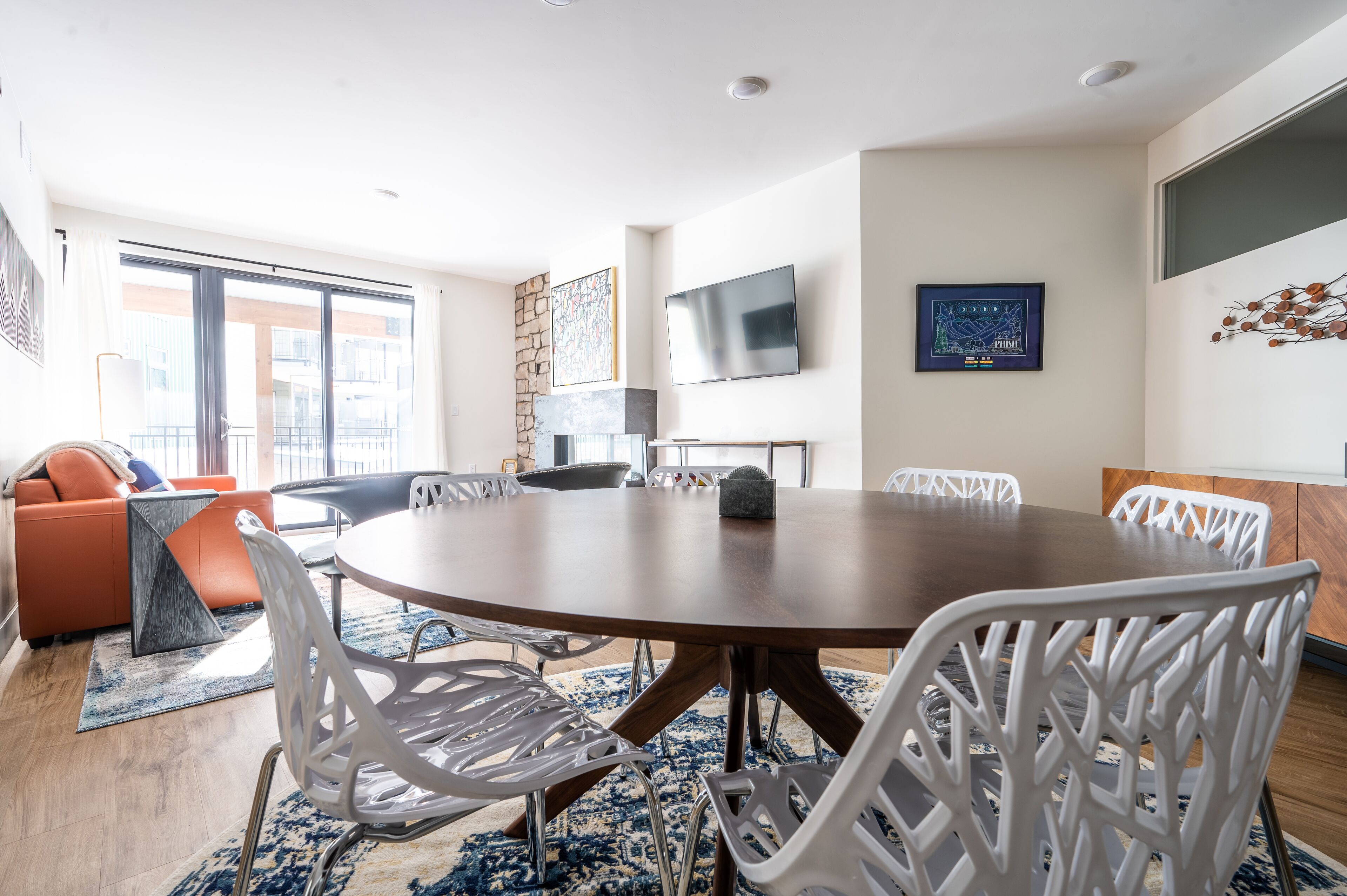 A modern dining area with a round table, white chairs, and a large window offering a view of the city.