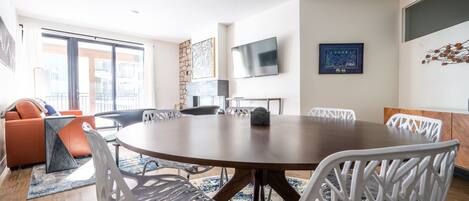 A modern dining area with a round table, white chairs, and a large window offering a view of the city.