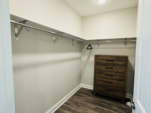Un dressing accessible sans porte, avec une commode en bois, des barres métalliques pour suspendre les vêtements et un plancher en bois.