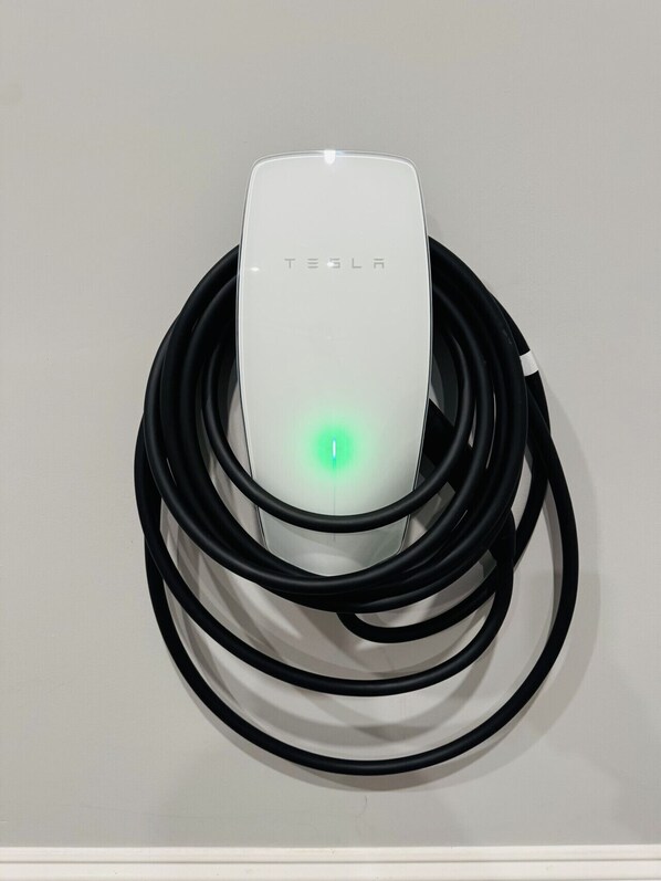 A Tesla charging station with a green light indicating charging status.