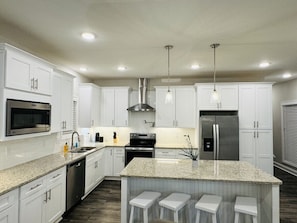 A modern kitchen with white cabinets, stainless steel appliances, granite countertops, and bar stools.