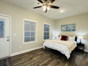 A bedroom with a bed, two bedside tables, a ceiling fan, and two windows with blinds.
