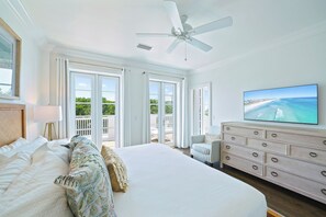 A spacious bedroom with a large bed, a ceiling fan, a television, and a view of the ocean through the balcony doors.