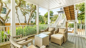 A covered outdoor seating area with wicker furniture and a glass-top table, surrounded by white railings and trees. - 1 Minute Stroll to Gulf with Private Heated Pool, Bikes, and a Gulf View (Santa Rosa Beach)