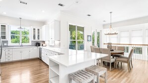 A spacious kitchen with white cabinetry, a central island, and a dining area with a wooden table and chairs. - 1 Minute Stroll to Gulf with Private Heated Pool, Bikes, and a Gulf View (Santa Rosa Beach)