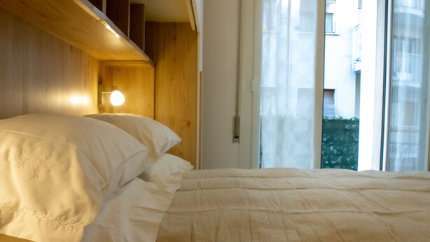 Ein Bett mit weißer Bettwäsche in einem Zimmer mit Holzvertäfelung und einem Fenster mit durchsichtigen Vorhängen.