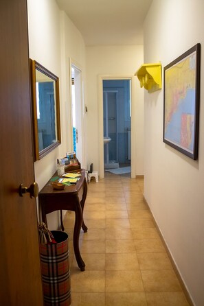 A hallway with a wooden door, a table with papers and a bottle, a mirror, and a map on the wall.