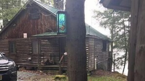 A rustic cabin with a wooden exterior, a visible chimney, and a small porch area. - Cabin on Sunset Lake W/Boathouse 
Separate Bunkhouse Rental
PET FRIENDLY  (Orwell)