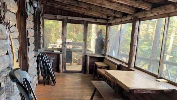 A rustic cabin interior with wooden walls, a stone fireplace, a rocking chair, and a dining area with benches and a table. - Cabin on Sunset Lake W/Boathouse 
Separate Bunkhouse Rental
PET FRIENDLY  (Orwell)