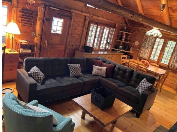 A cozy log cabin interior with a dark leather sofa, a wooden coffee table, and a blue armchair.