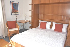 Ein Hotelzimmer mit einem großen Bett, einem Sessel, einem Schreibtisch und einem an der Wand befestigten Regal.