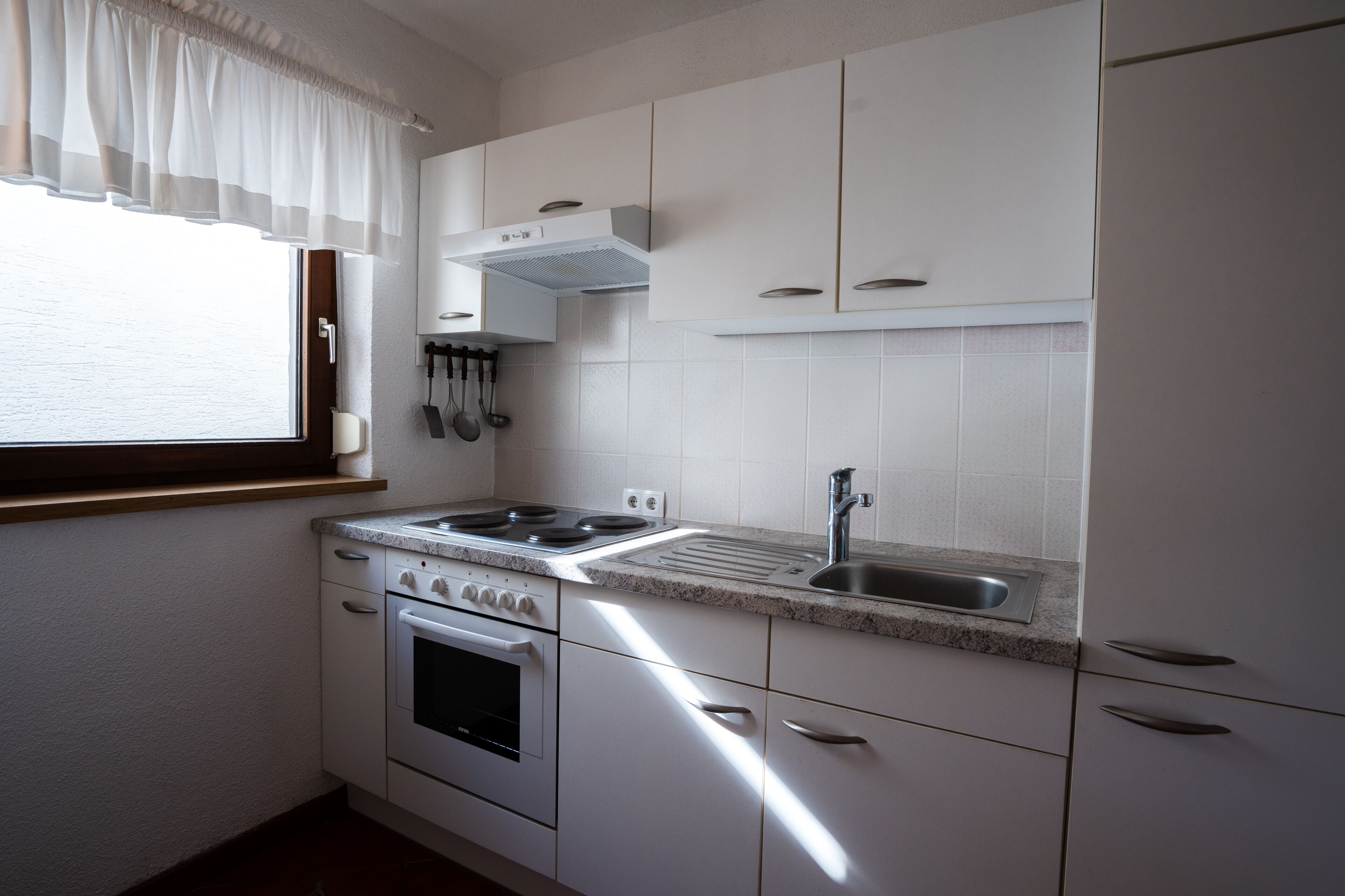 A kitchen with white cabinets, a stove, a sink, and a window with a white valance.