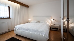 A bedroom with a large bed, bedside tables, a mirror, and a window with curtains. - spacious apartment with nice view of the Tyrolean mountains (Reith bei Seefeld)