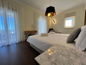 Een hotelkamer met een groot bed, een nachtkastje van marmer, een bureau en een raam met gordijnen.