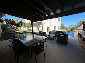 Een terras buiten met een tafel met glazen blad, zwarte stoelen en een bank.