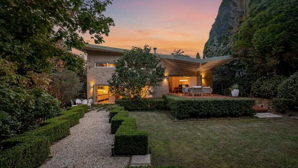 Ein modernes Haus mit gepflegtem Garten, einem Kiesweg und einer Terrasse mit Gartenmöbeln.
