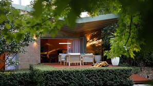 Ein modernes Haus mit Backsteinfassade, einer überdachten Terrasse mit Gartenmöbeln und einem gepflegten Garten.