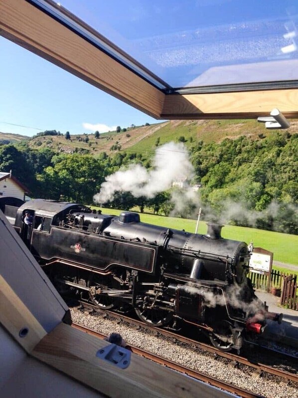 A steam locomotive on tracks with a scenic view of green hills and a clear sky.