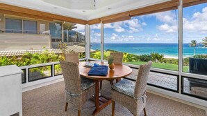 Ein Balkon mit Holztisch und Korbstühlen, mit Blick auf einen tropischen Strand und Ozean.