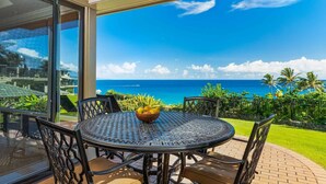 Ein runder Tisch mit Stühlen und einer Obstschale, mit Blick auf die Küste, Palmen und das Meer.