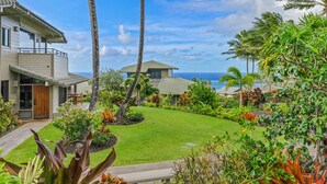 A residential property with a well-maintained lawn, tropical plants, and a view of the ocean.