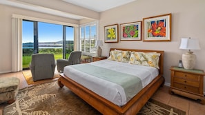 A spacious bedroom with a large bed, a chair, a nightstand, and a view of the outdoors.