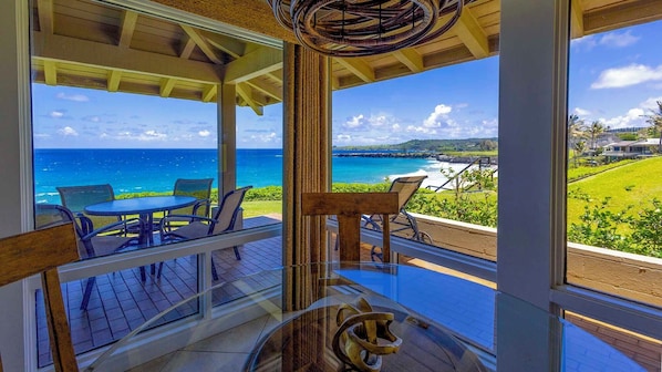 A glass-enclosed balcony with a view of the ocean and a grassy area.
