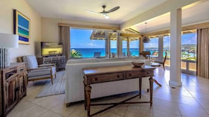 A spacious living room with a large window overlooking the ocean, a ceiling fan, and a dining area with a view.