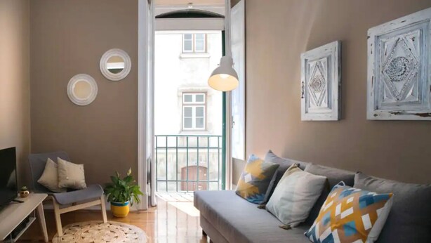 A living room with a grey sofa, a TV, a chair, and a potted plant. - Lisbon Liberdade Central Apartment 1E (Lisboa)