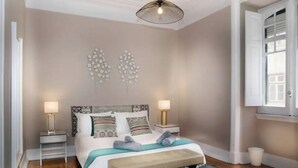 A bedroom with a bed, two bedside tables, a bench, a hanging light fixture, and a window with shutters. - Lisbon Liberdade Central Apartment 1E (Lisboa)