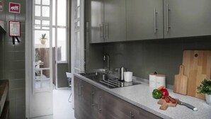 A modern kitchen with grey cabinets, a stainless steel sink, and a wooden cutting board with vegetables and a knife on the counter. - Lisbon Liberdade Central Apartment 1E (Lisboa)