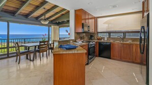 Cozinha com vista para o oceano, armários de madeira, bancada de granito e um espaço de jantar com cadeiras.