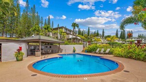 Uma piscina com borda de tijolos, rodeada por espreguiçadeiras e uma área coberta com churrasqueira.