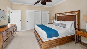 Um quarto com cama de madeira, roupa de cama branca, manta azul, mesa de cabeceira, luminária e cômoda.
