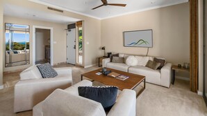 Un salon spacieux, doté d’un grand canapé, d’une table basse et d’un ventilateur de plafond. Une grande fenêtre offre une vue sur l’extérieur.