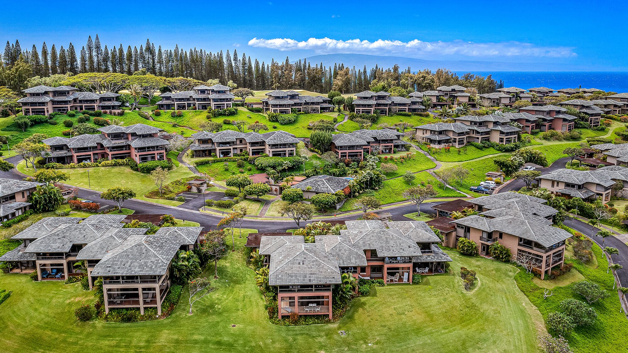 A resort with multiple buildings, lush green lawns, and a view of the ocean.