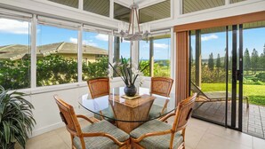 A dining area with a glass table, wicker chairs, and a vase with flowers.