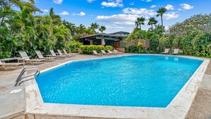 Une piscine rectangulaire à l’eau d’un bleu cristallin, entourée de chaises longues et de palmiers.