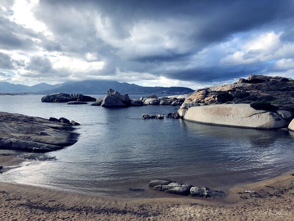Experience the serene coastal landscape with a rocky shoreline, sandy beach, and breathtaking mountain views.
