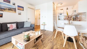 A modern living room with a grey sofa, wooden coffee table, and a dining area with white chairs and a glass table. - Occi - proche plage - One Bedroom Apartment, Sleeps 4 (L'Île-Rousse)
